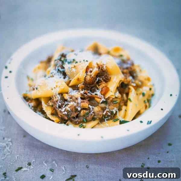 A white bowl filled with pappardelle pasta with meat sauce sprinkled with chopped rosemary.