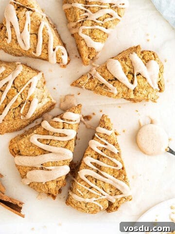 White surface with several triangles of glazed cinnamon scones. Spoon and cinnamon sticks.