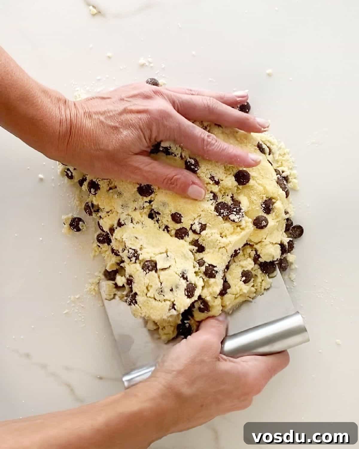 Irresistible Chocolate Chip Scones Recipe for Perfect Breakfast 5 Using dough scraper to form chocolate chip dough for scones. White marbled surface.