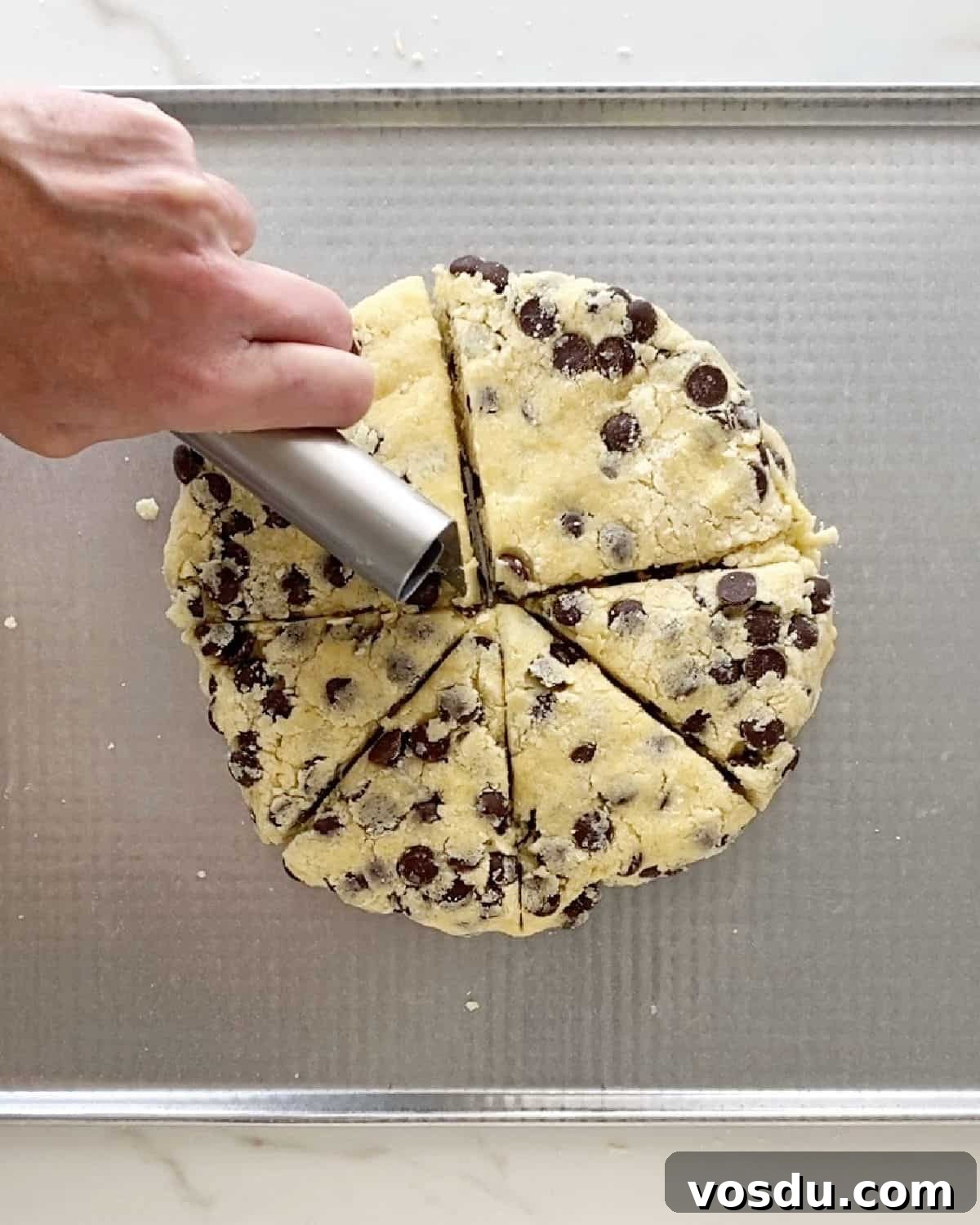 Irresistible Chocolate Chip Scones Recipe for Perfect Breakfast 6 Cutting triangles with a dough scraper from round chip scone dough on a cookie sheet.