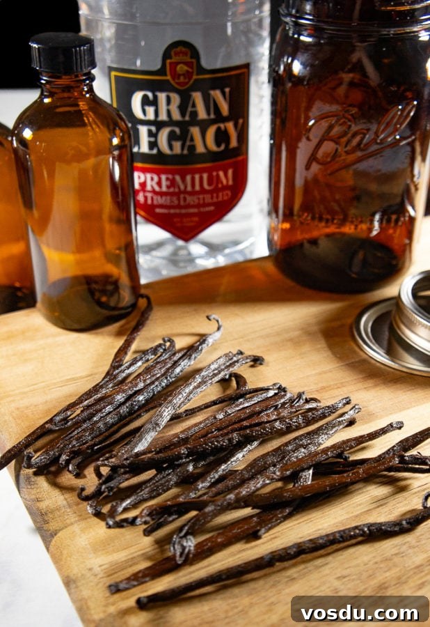 a pile of vanilla beans on a wooden cutting board with brown glass bottles behind it and a bottle of vodka