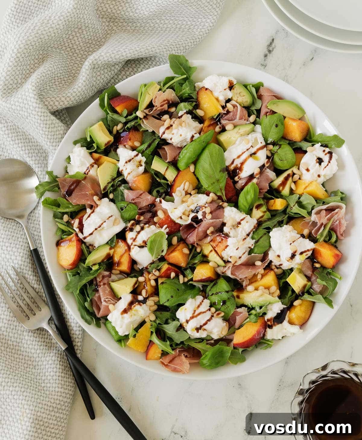 Summer Peach Burrata Salad with Prosciutto and Arugula 2 A colorful burrata and peach salad with greens, avocado, basil, and nuts in a white salad bowl.