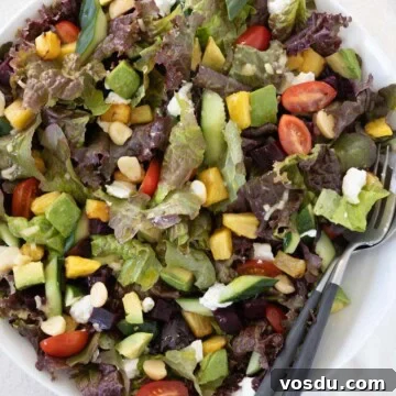 Color Hawaiian salad with tomatoes, avocado, pineapple, beets. macadamia nuts and more in a bowl with utensils.