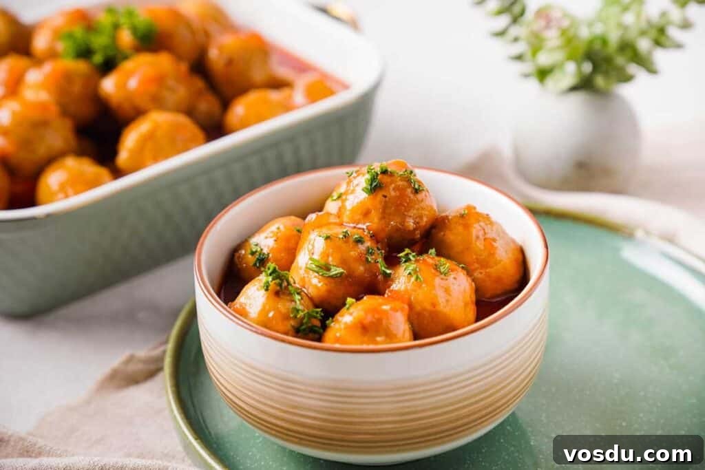 Slow-Cooker Apple Jelly Meatballs for Party Appetizers 2 apple jelly meatballs in bowl on table with more in the background