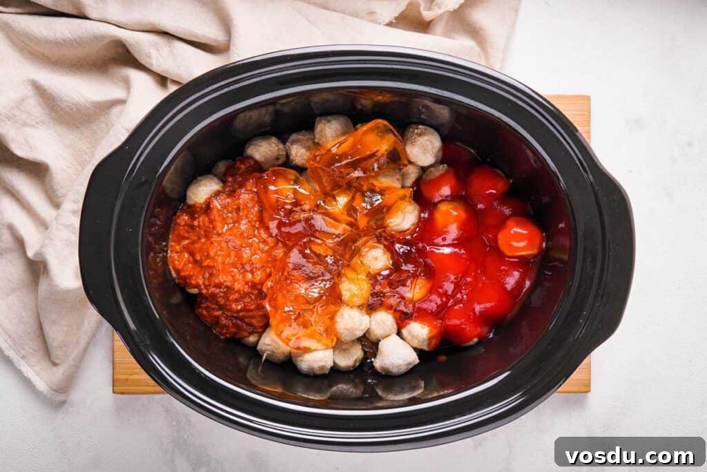 Slow-Cooker Apple Jelly Meatballs for Party Appetizers 3 meatballs in a slow cooker topped with apple jelly, pizza sauce, and ketchup