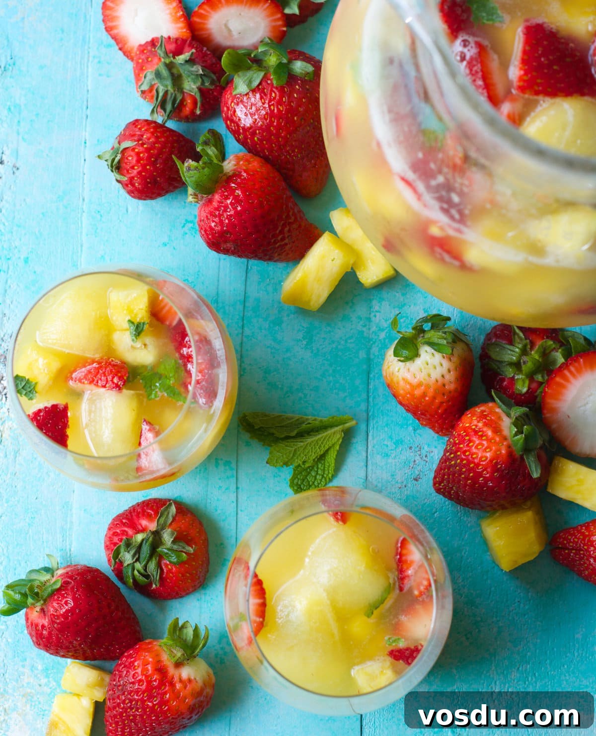 Sparkling Pineapple Punch Recipe with Video Tutorial 3 Overhead view of two glasses of non alcoholic punch, a pitcher of punch, and fresh fruit.