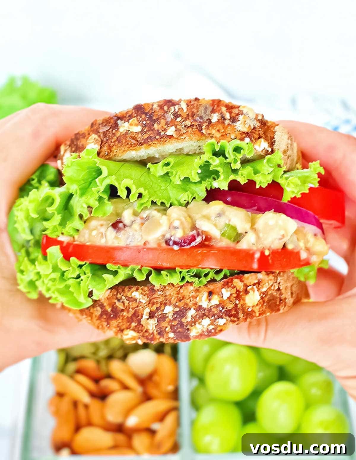 Flavorful Vegan Chickpea Salad with Lemon Herb Dressing 2 Two hands holding a sandwich with lettuce, tomatoes, onion, and chickpea salad.