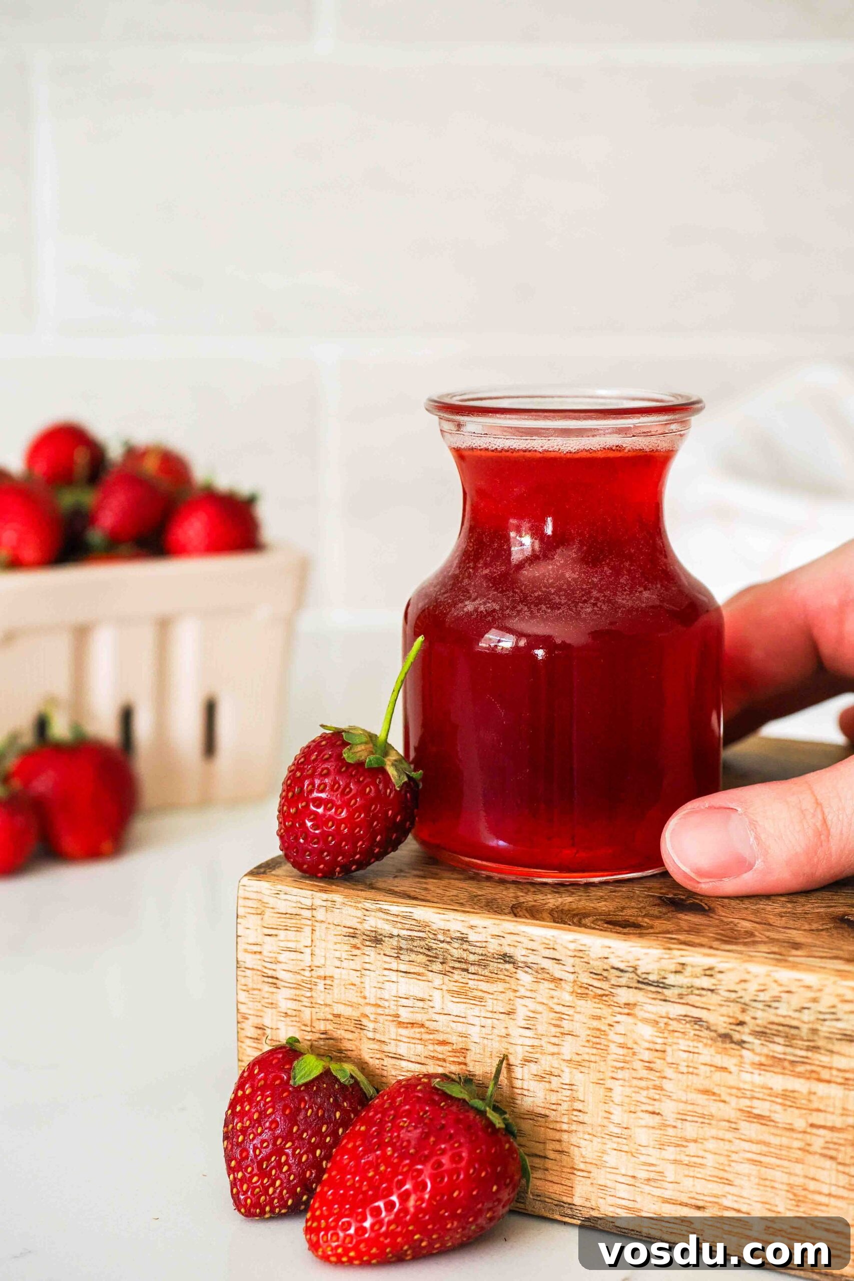 Homemade Small-Batch Strawberry Syrup Recipe 2 A hand holds a small jar of strawberry syrup.