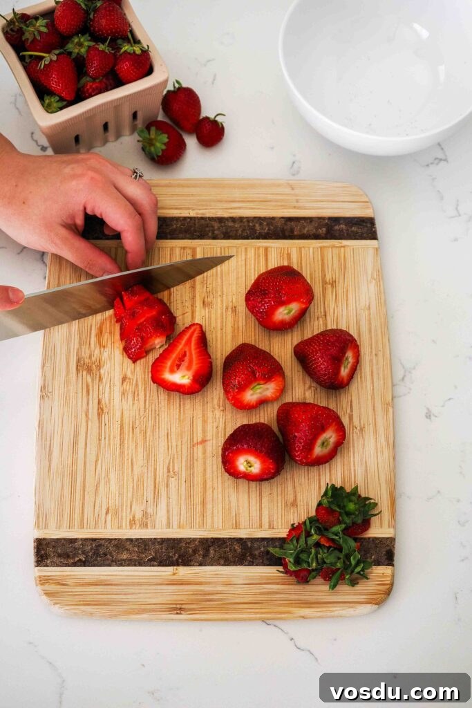 Homemade Small-Batch Strawberry Syrup Recipe 4 A knife dices strawberries on a wooden cutting board.