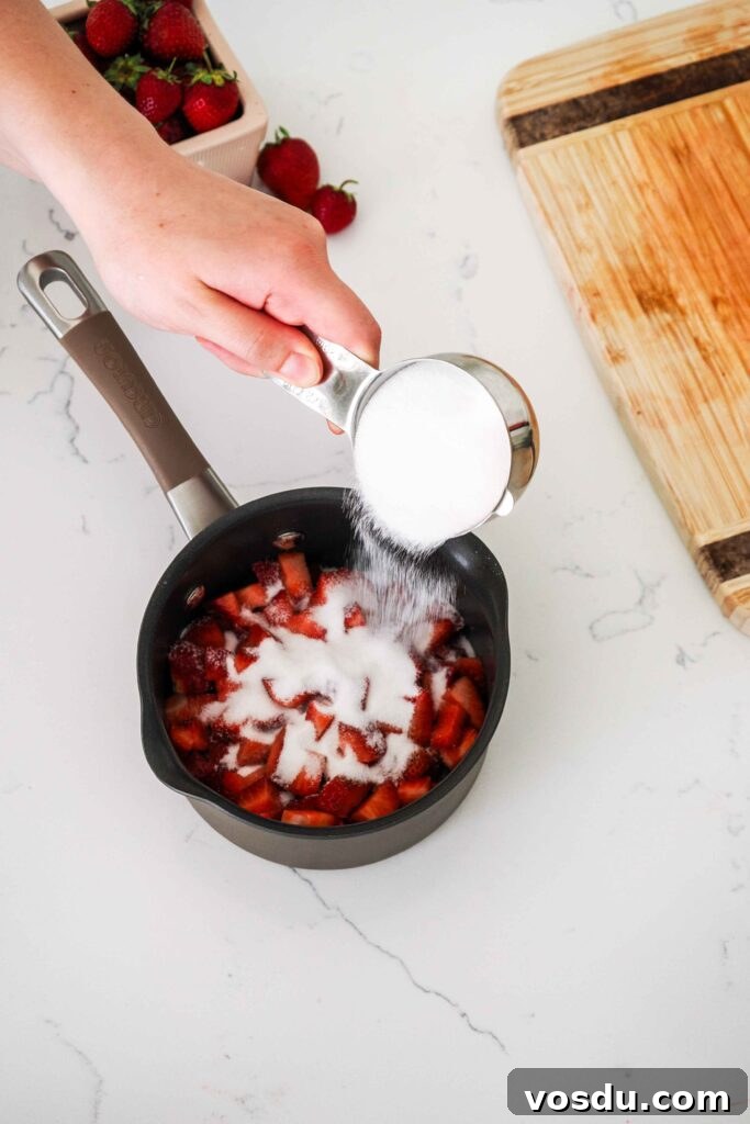 Homemade Small-Batch Strawberry Syrup Recipe 6 Sugar is poured onto diced strawberries in a small saucepan.