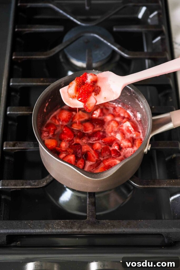 Homemade Small-Batch Strawberry Syrup Recipe 7 A spatula holds up softened strawberries in a small pot over the stove.