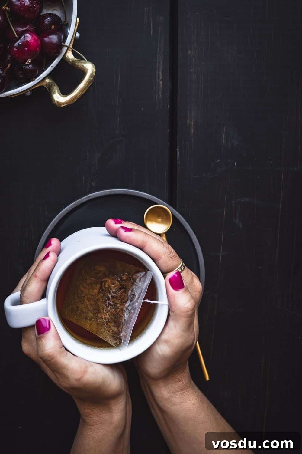 Top San Francisco Coffee Shops for Digital Nomads — 2026 Guide 2 Hands with pink nails cradling a white mug of tea with a gold spoon on a dark background.
