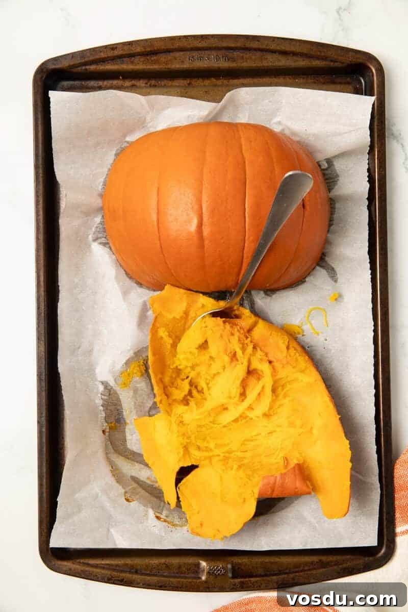 Homemade Pumpkin Puree From Scratch — Step-by-Step Recipe 6 a baked pie pumpkin on a baking sheet. The flesh is being pulled back.