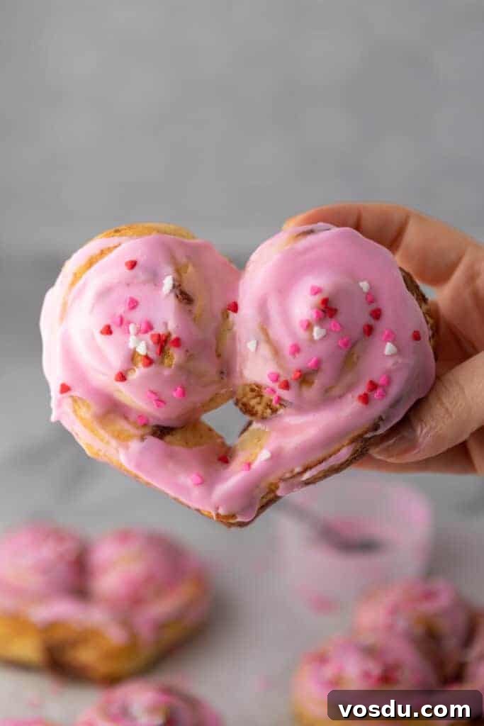 Heart-Shaped Cinnamon Rolls for Valentine’s Day Using Canned Dough 2 Heart-shaped cinnamon roll with pink frosting and Valentine’s sprinkles held in hand