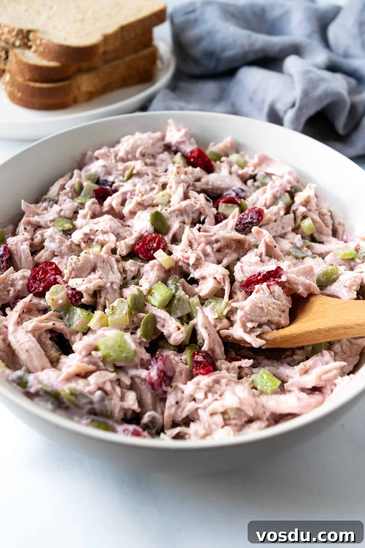 Cranberry Turkey Salad Recipe for Holiday Leftovers 8 A scoop of Cranberry Turkey Salad on a wooden spoon from a white bowl.