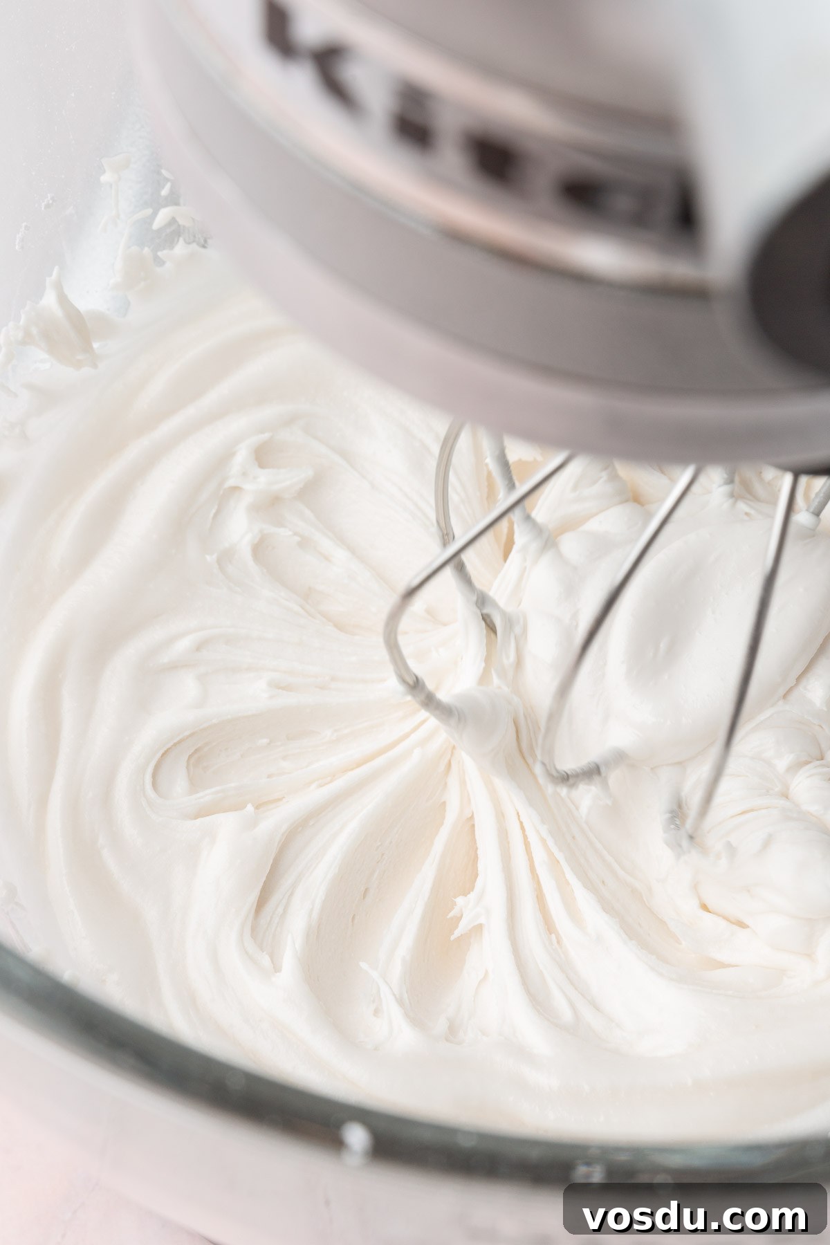Perfect Royal Icing Recipe: Smooth, Glossy, and Pipe-Ready 78 A stand mixer with a glass mixing bowl with the whisk attachment mixing a bowl of white royal icing.