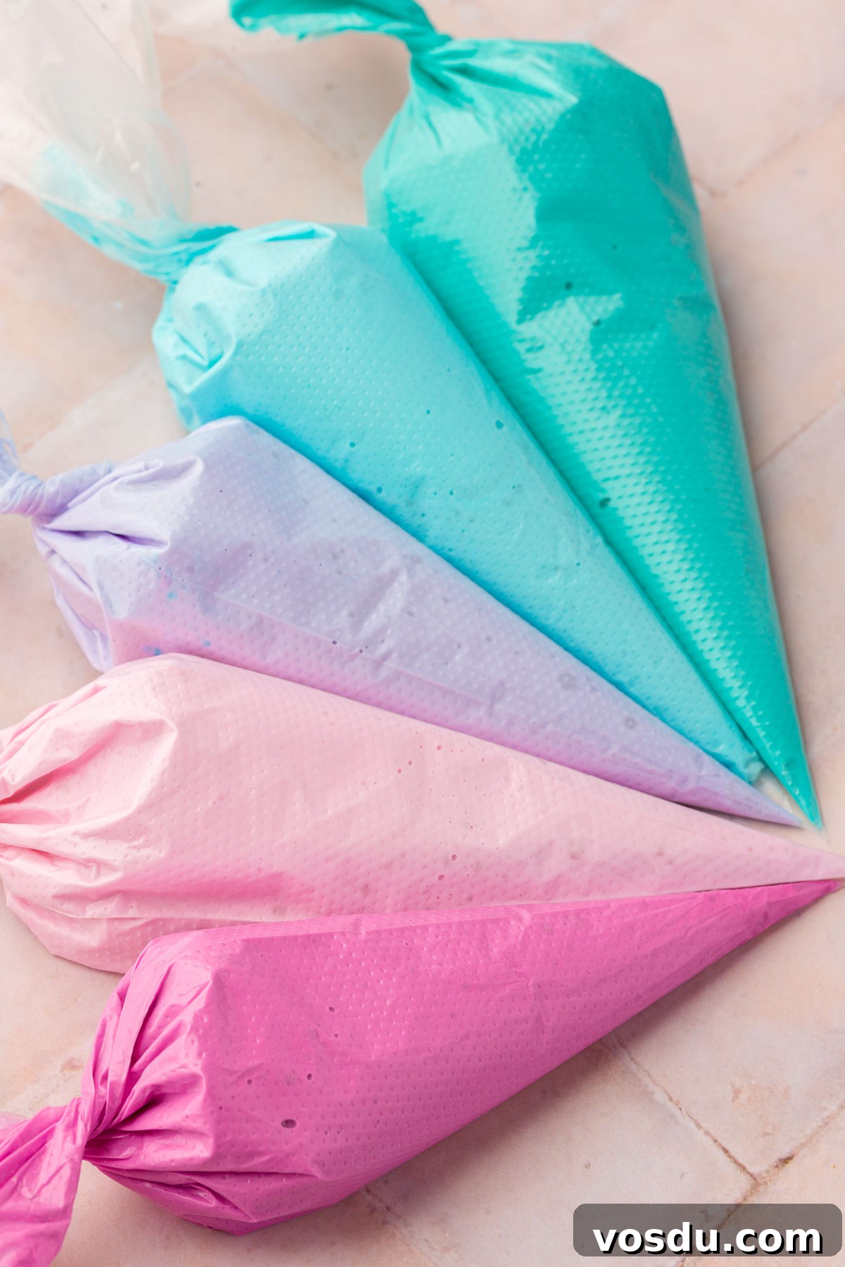 Perfect Royal Icing Recipe: Smooth, Glossy, and Pipe-Ready 12 Five disposable pastry bags filled each with a different color of royal icing, teal, blue, purple, light pink and fuchsia.
