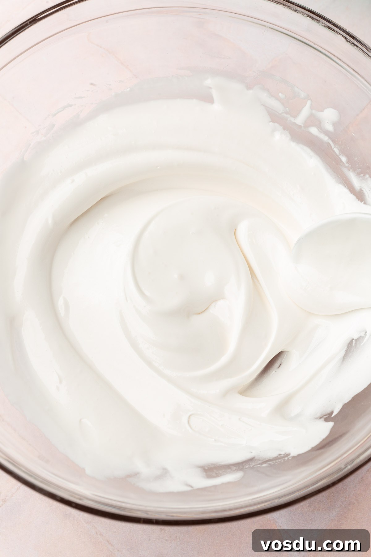 Perfect Royal Icing Recipe: Smooth, Glossy, and Pipe-Ready 13 A glass mixing bowl with thinned out white royal icing in it with a spoon.