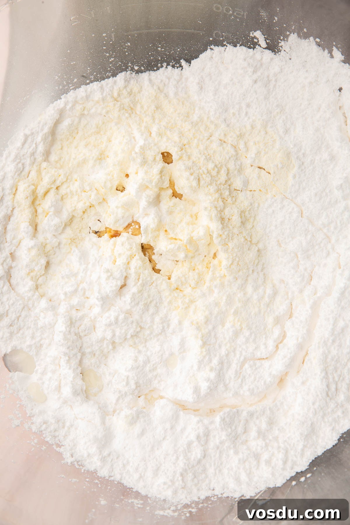 Perfect Royal Icing Recipe: Smooth, Glossy, and Pipe-Ready 4 A glass mixing bowl with powdered sugar, vanilla, water, and meringue powder before mixing together.