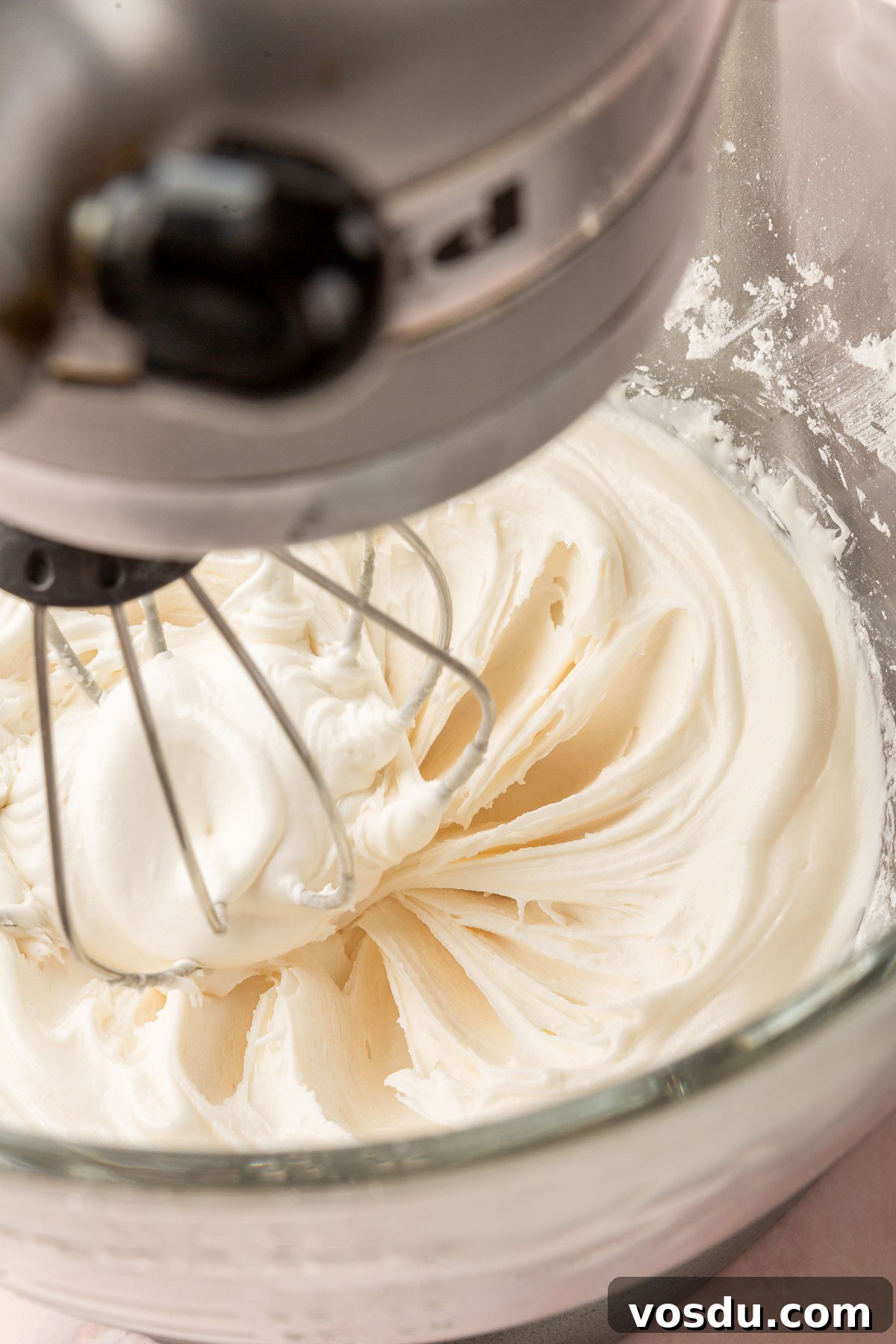 Perfect Royal Icing Recipe: Smooth, Glossy, and Pipe-Ready 5 A stand mixer with a glass mixing bowl with the whisk attachment mixing a bowl of white royal icing.