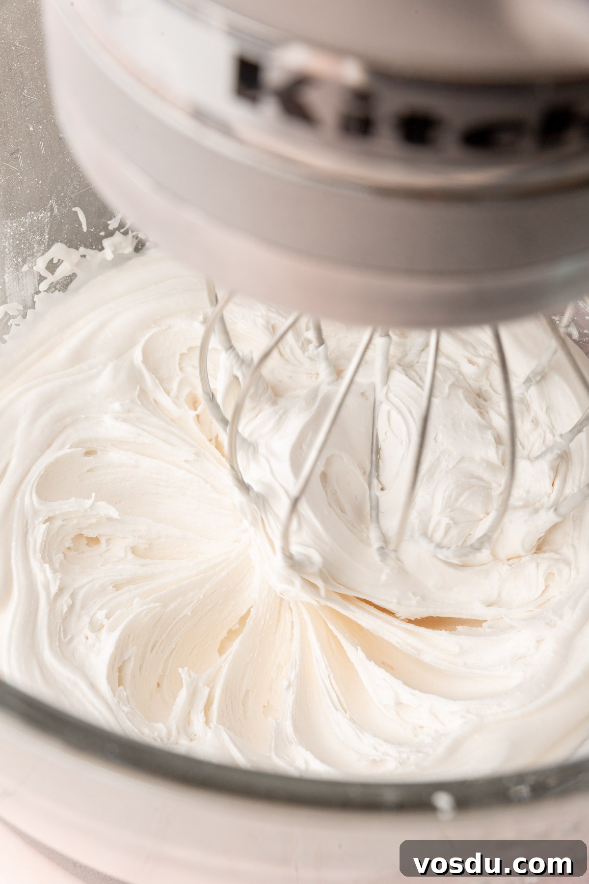 Perfect Royal Icing Recipe: Smooth, Glossy, and Pipe-Ready 6 A stand mixer with a glass mixing bowl with the whisk attachment mixing a bowl of white royal icing.