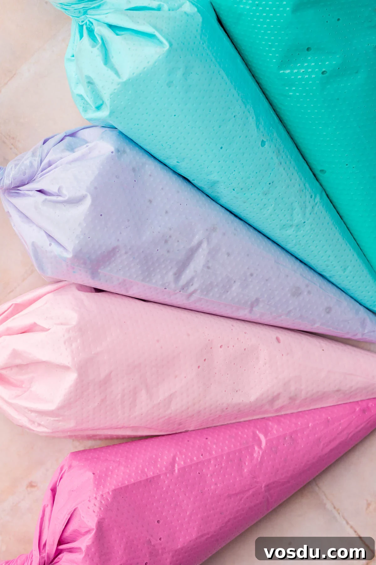 Perfect Royal Icing Recipe: Smooth, Glossy, and Pipe-Ready 9 Five disposable pastry bags filled each with a different color of royal icing, teal, blue, purple, light pink and fuchsia.