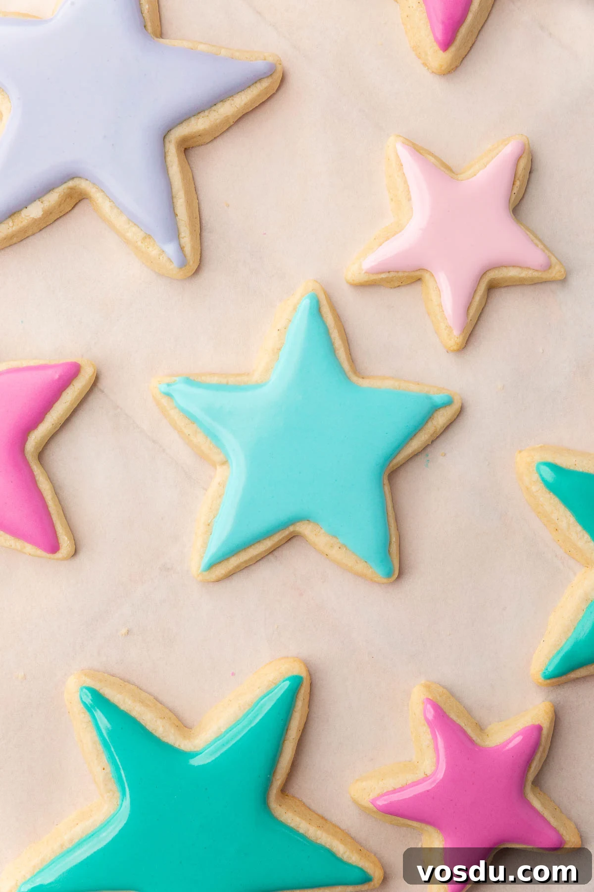 Perfect Royal Icing Recipe: Smooth, Glossy, and Pipe-Ready 10 Star sugar cookies frosted with pink, purple, blue and green royal icing that is still wet.
