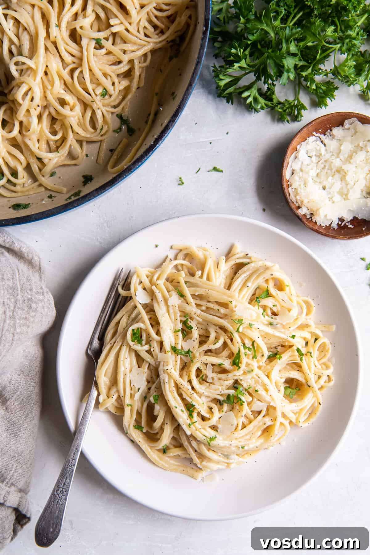 Creamy Parmesan Noodles with Garlic and Herbs 6 A top down shot of Parmesan Noodles in a skillet and on a white plate with a fork.