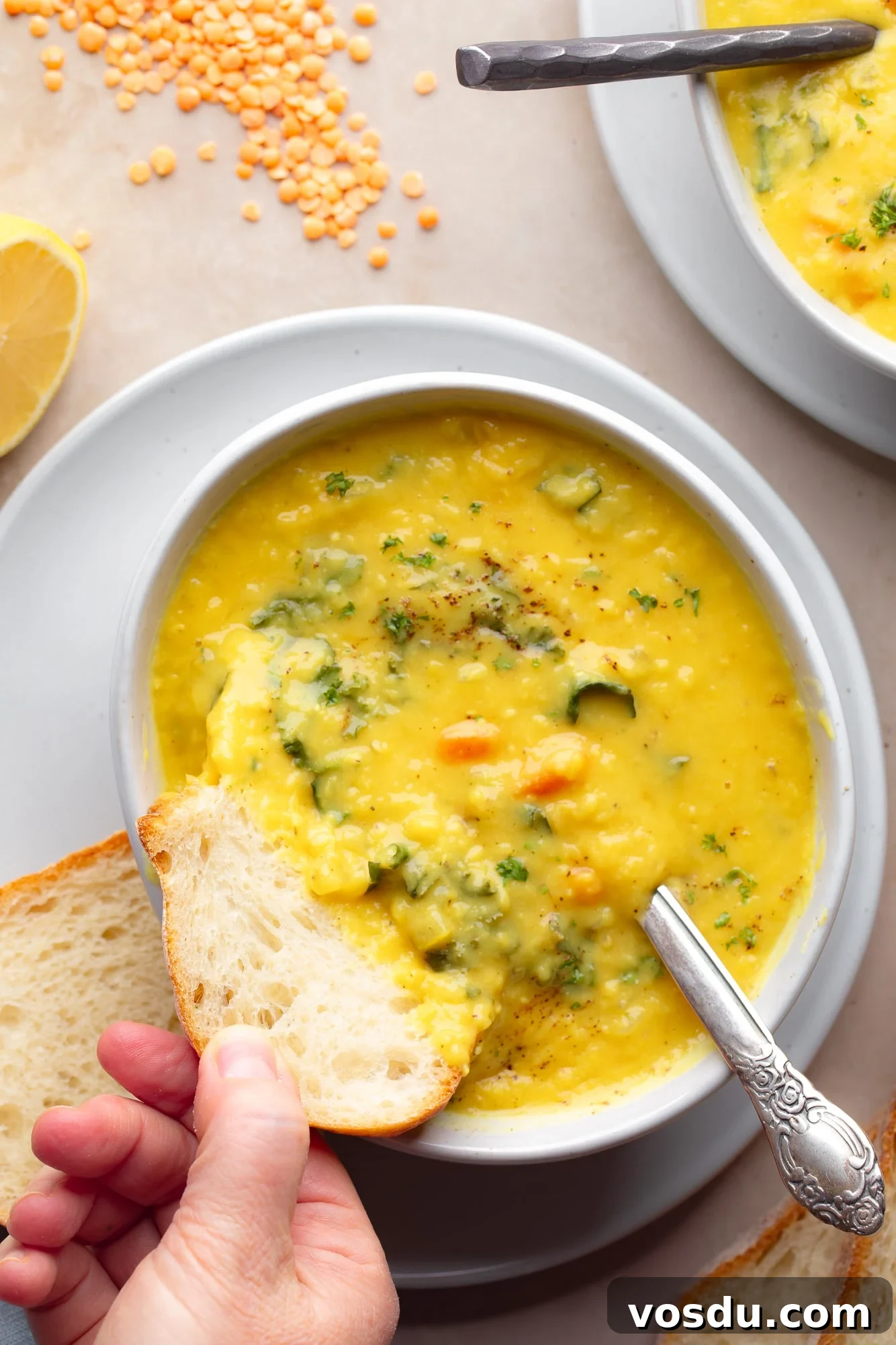 Zesty Lemon Lentil Soup Recipe for Bright, Comforting Meals 2 a womans hand dipping a piece of bread into a bowl of lemon lentil soup.