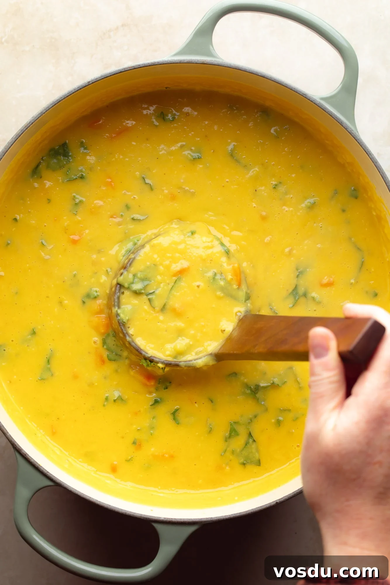 Zesty Lemon Lentil Soup Recipe for Bright, Comforting Meals 3 a womans hand lifting a wooden ladle from a pot of lemon lentil soup.