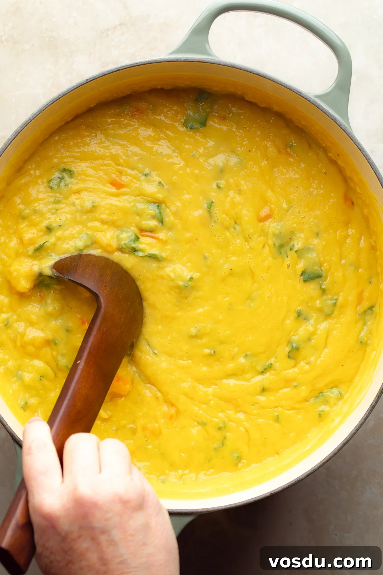 Zesty Lemon Lentil Soup Recipe for Bright, Comforting Meals 8 a womans hand stirring a wooden ladle in a pot of lemon lentil soup.