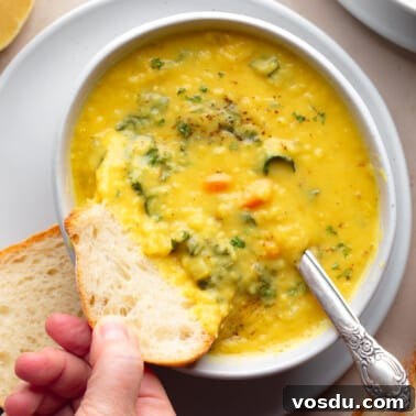 Zesty Lemon Lentil Soup Recipe for Bright, Comforting Meals 10 a womans hand dipping a piece of bread into a bowl of lemon lentil soup.