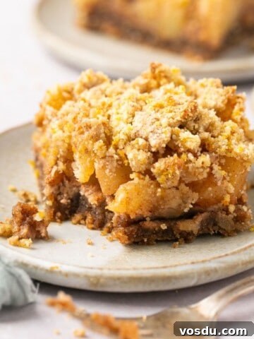 A healthy apple crumble bar on a plate with a bite taken out of it and a fork beside it.