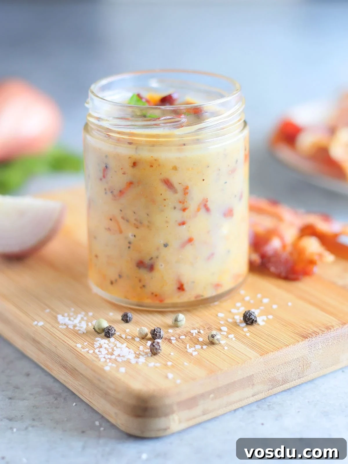 Savory Warm Bacon Vinaigrette for Salads and Vegetables 15 Jar of hot bacon dressing on a wooden cutting board with a sliced shallot and bacon slices in the background.
