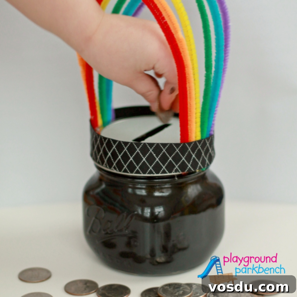 10 Creative DIY Piggy Banks You Can Make at Home 11 A hand putting a coin inside a pot o’ gold piggy bank with rainbow holder