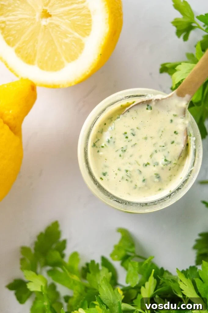 A jar of pale sauce next to lemons and cilantro on a white background.