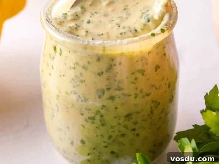 A spoon dipping into a glass jar with herby sauce in it.