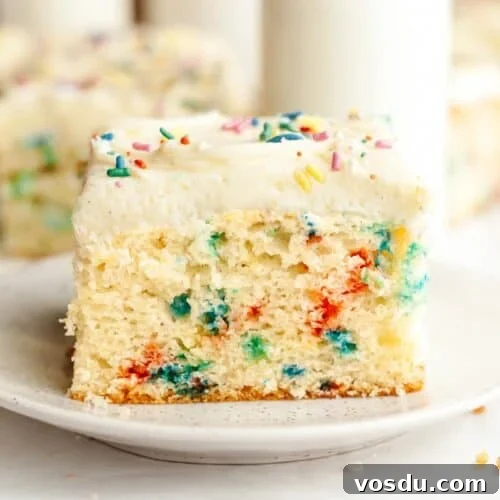 A slice of confetti sheet cake with vanilla frosting on a small plate.