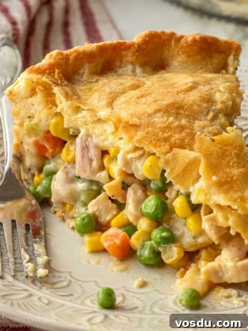 Slice of baked chicken pot pie on white plate with fork.