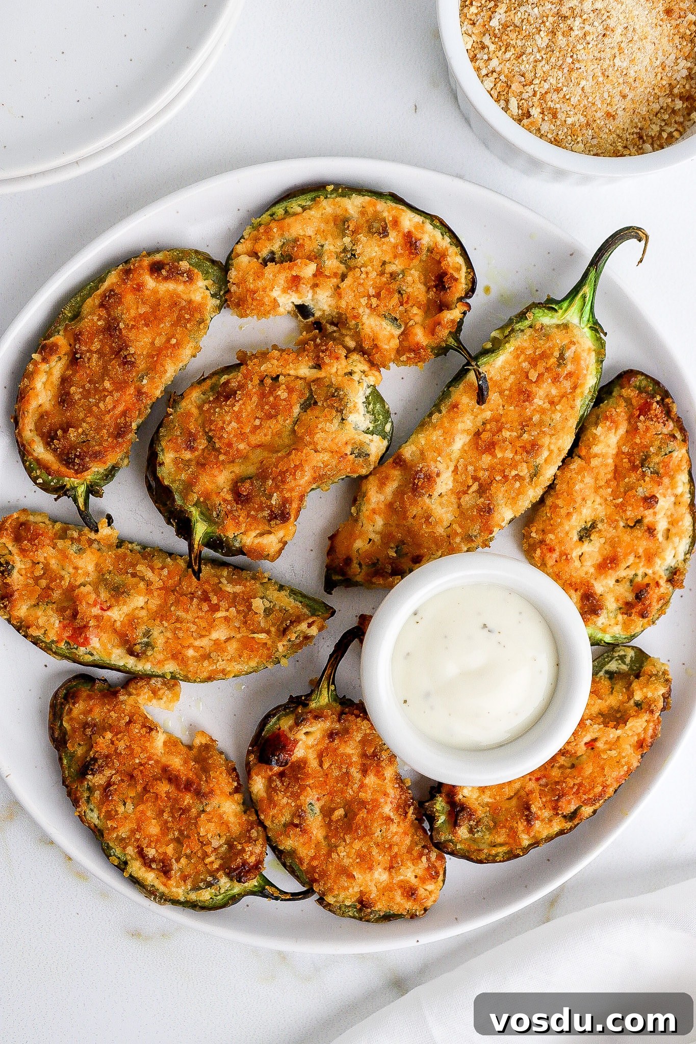 Spicy jalapeno poppers on white plate with ranch dressing on the side.