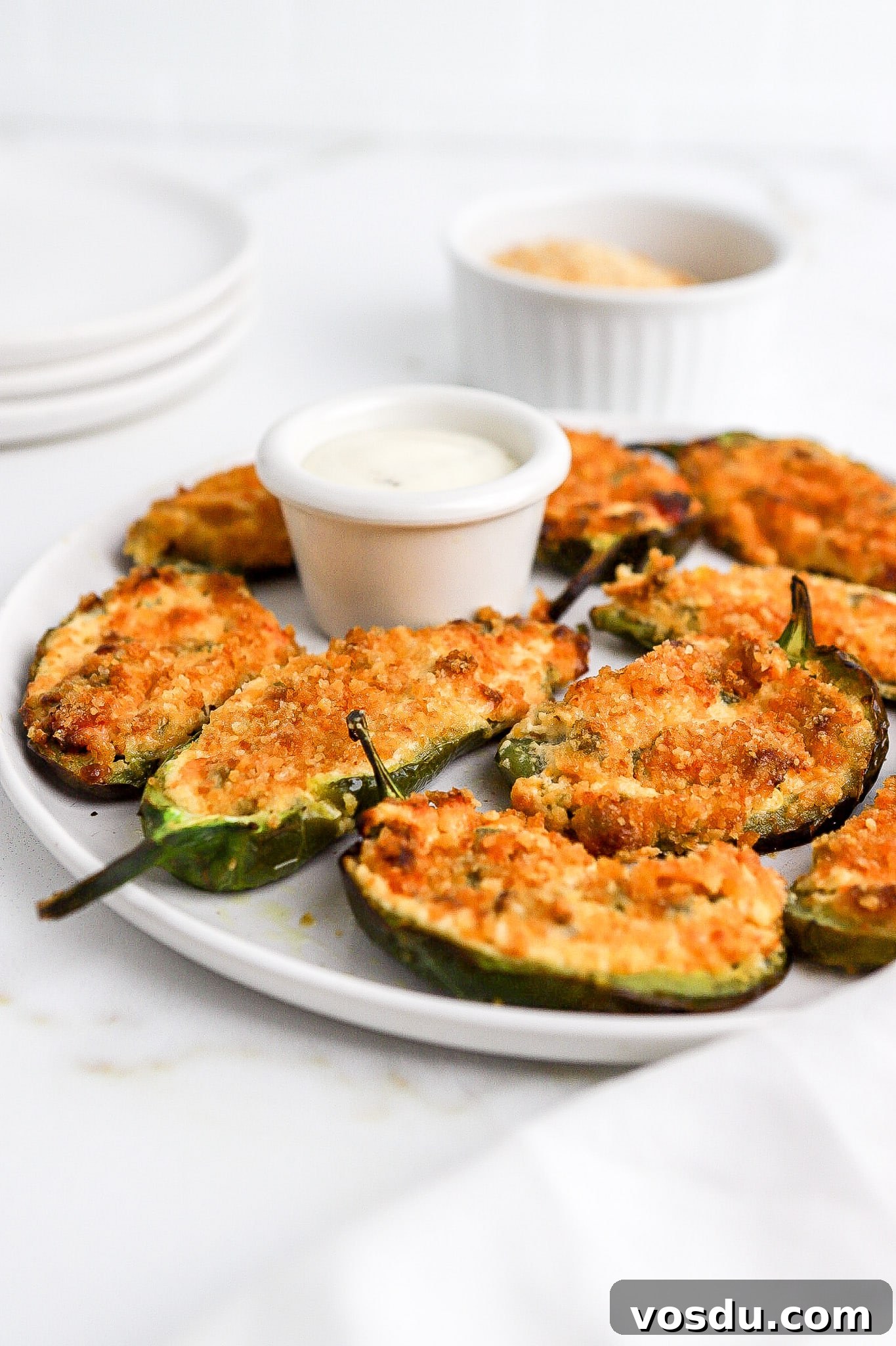 Side view of air fryer jalapeno poppers with ranch dressing for dipping on white plate.