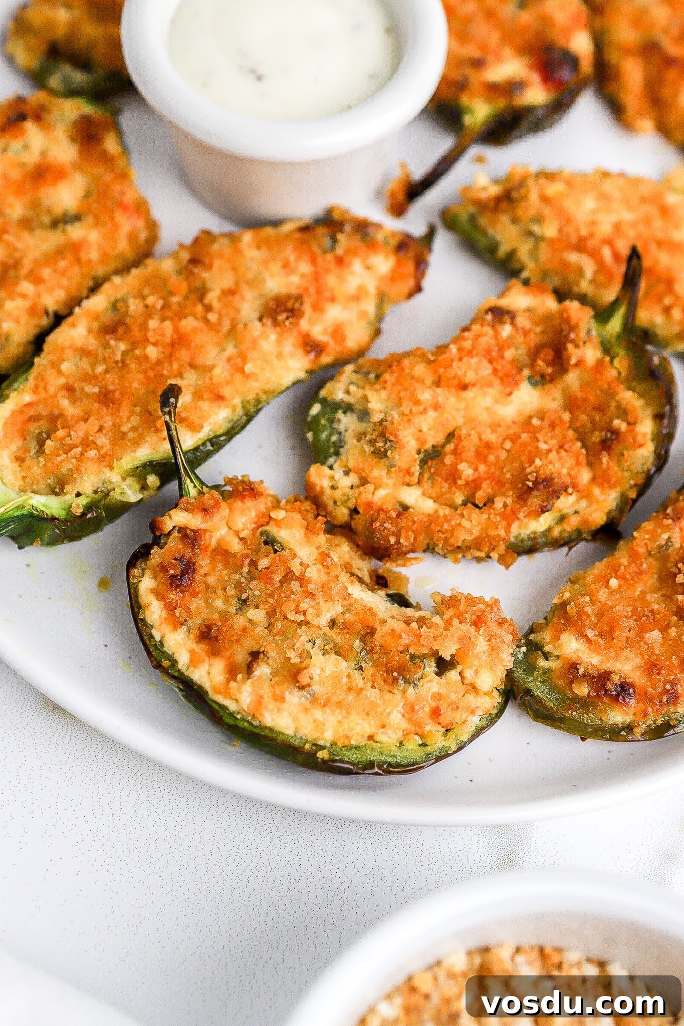 Side view of jalapeno poppers on small white plate with ranch dressing for dipping.