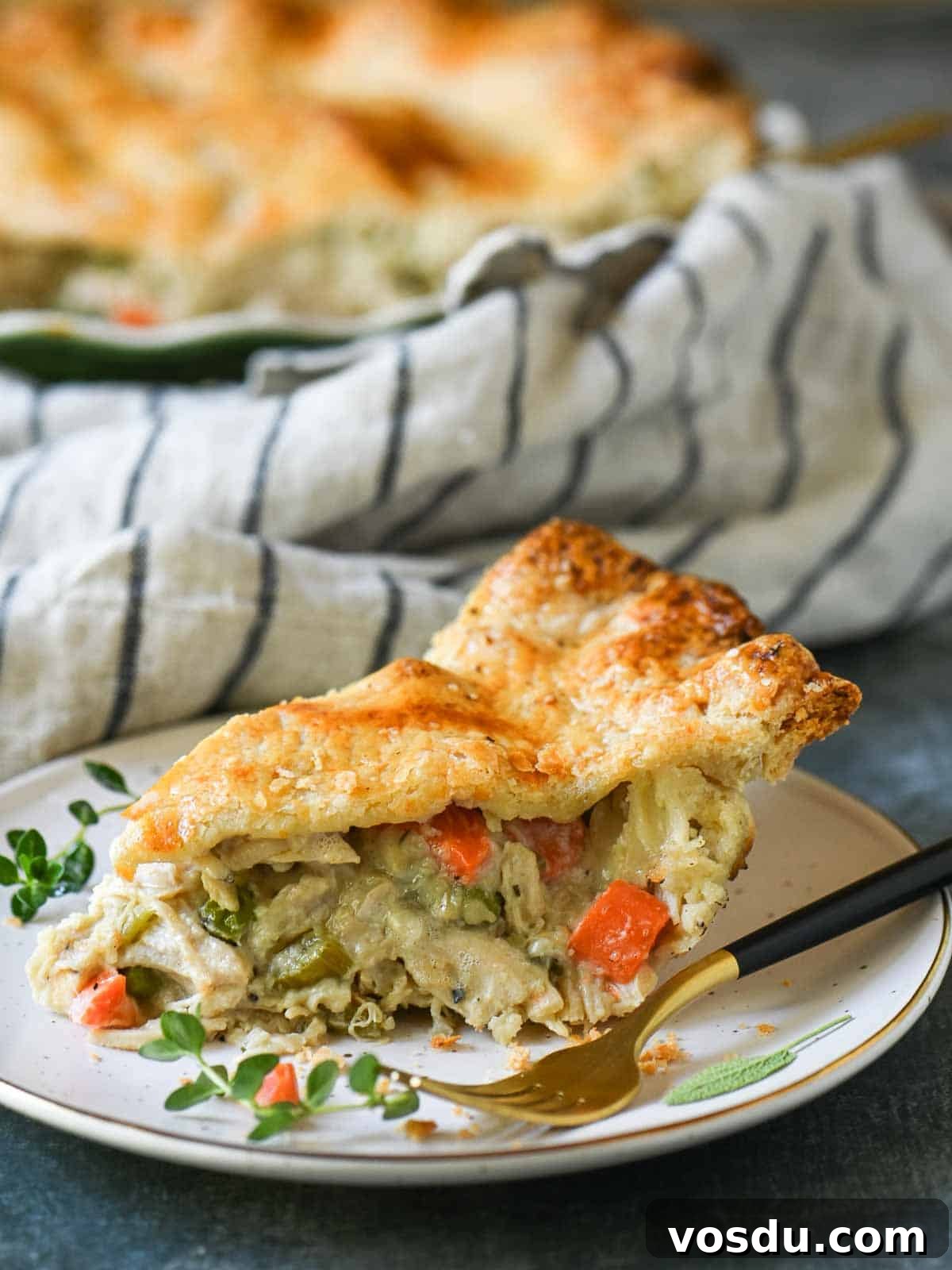 A slice of chicken pot pie on a white plate with herbs and a fork.