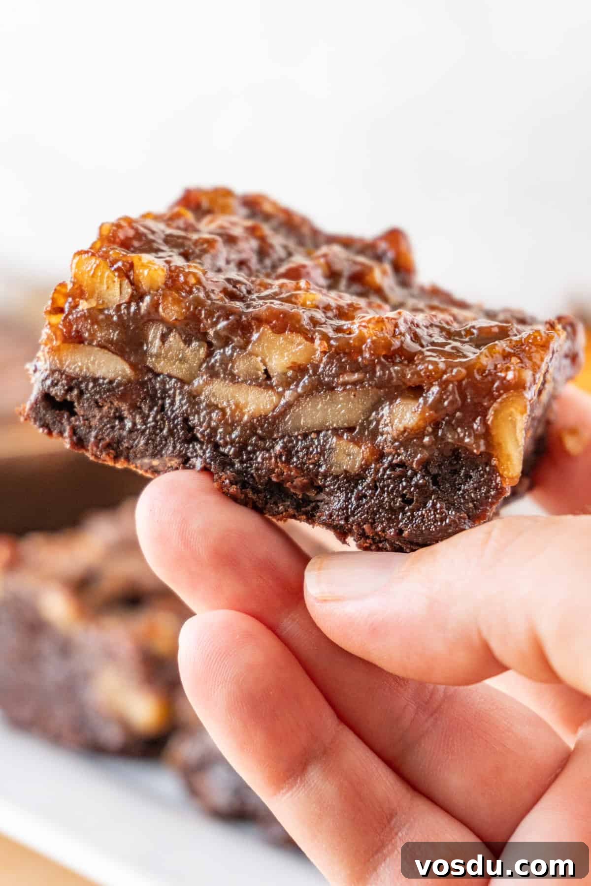 Holding a Pecan Pie Brownie in hand, showing a beautiful cross-section of the brownie topped with pecan pie filling.