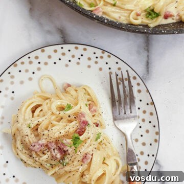 A plate of spaghetti carbonara sprinkled with black pepper.