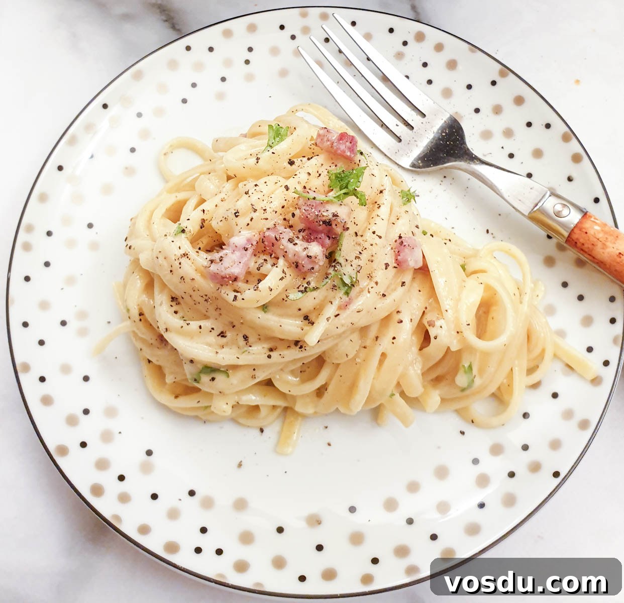 A helping of creamy spaghetti carbonara on a plate with a fork.