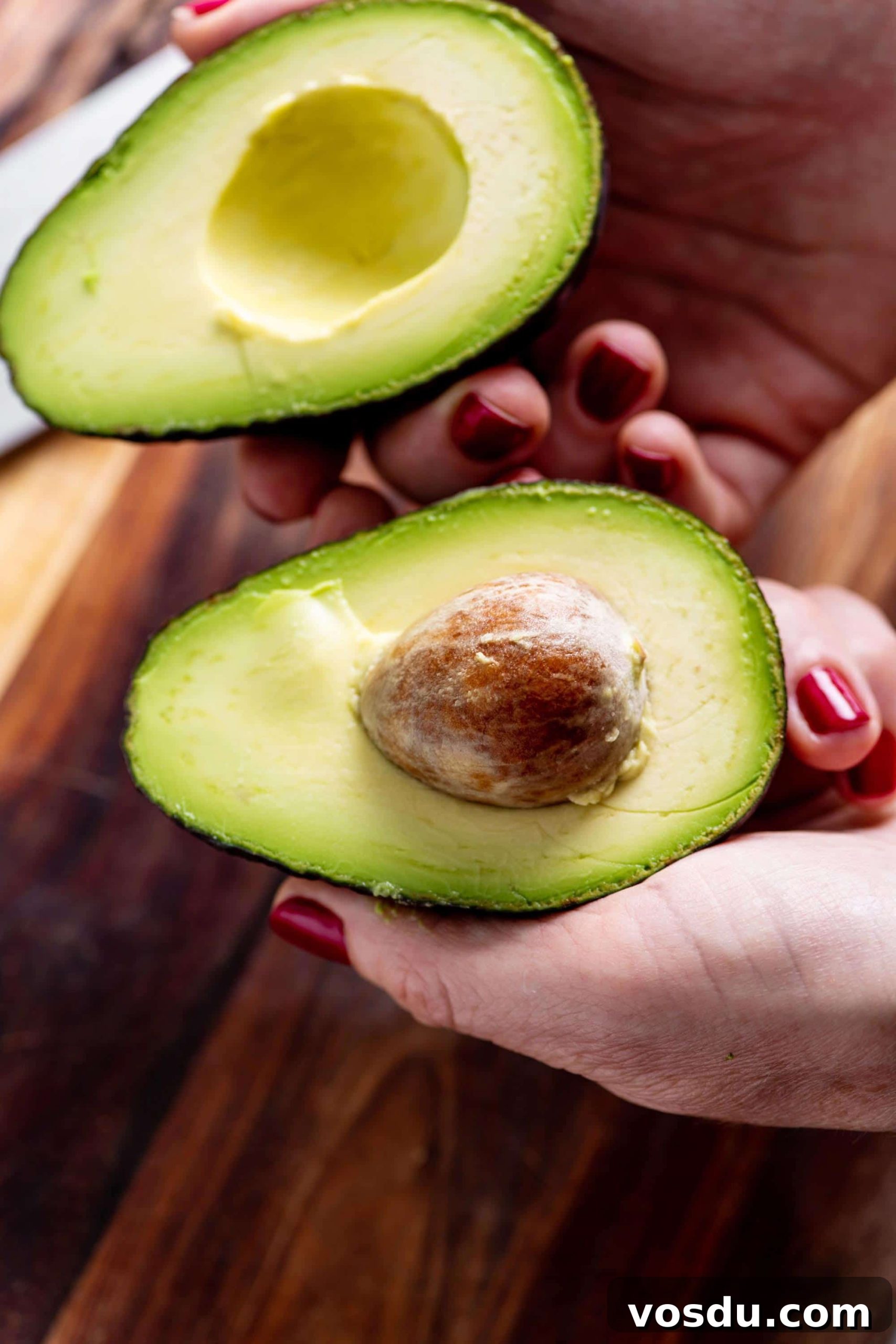 Woman holding avocado cut in half.