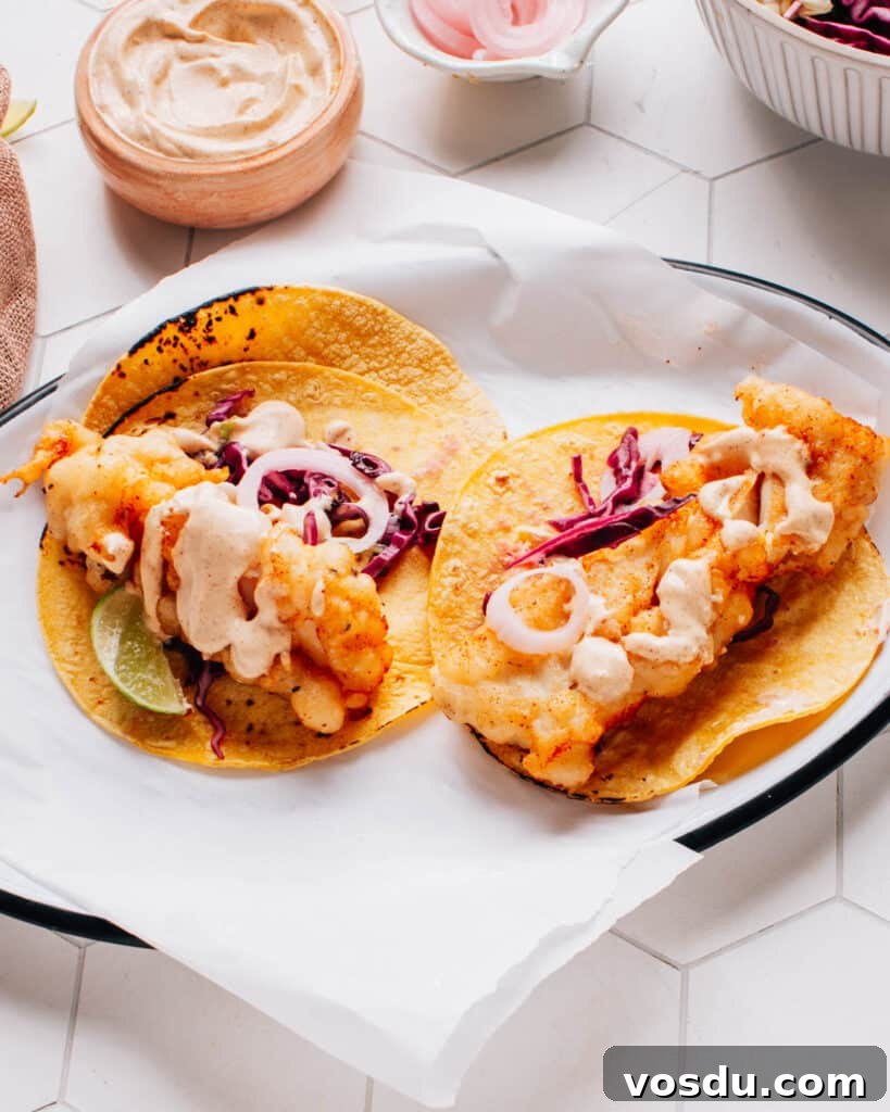 Two delicious Baja fish tacos artfully presented on parchment paper, drizzled with flavorful Baja sauce and accompanied by a bed of crispy cabbage slaw.