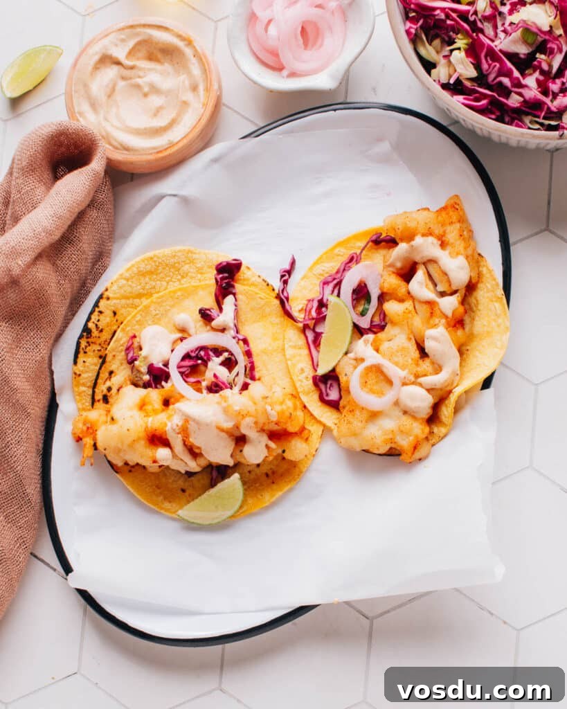 Two delicious Baja fish tacos artfully presented on parchment paper, drizzled with flavorful Baja sauce and accompanied by a bed of crispy cabbage slaw.
