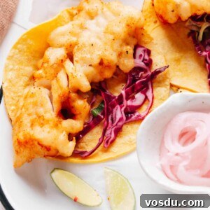 Baja fish tacos artfully presented on parchment paper, drizzled with flavorful Baja sauce and accompanied by a bed of crispy cabbage slaw.